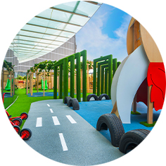 Outdoor playground with a toy road, green obstacles, black tires, and a large rocket structure under a transparent roof.
