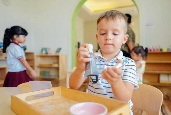 A young boy is playing with a tray in a classroom.
