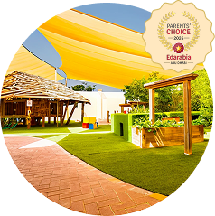 Outdoor playground with artificial grass, wooden play structures, and shade sails. A 