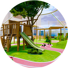 Playground with a wooden treehouse, a green slide, winding pink paths, and plants, set in an outdoor area on artificial grass.