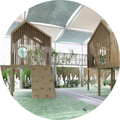 Modern outdoor playground with wooden climbing structures, rope bridge, and shade canopy, surrounded by greenery and artificial grass.