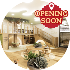Modern indoor playroom with wooden furniture, plants, a staircase, and an “Opening Soon” badge in the top right corner.